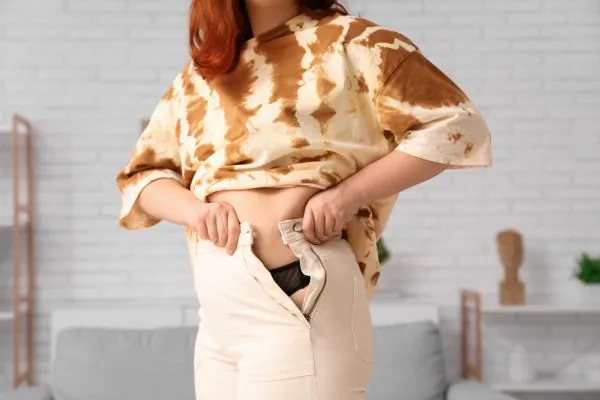 Image of woman trying to do her trousers up after pregnancy weight gain Brentwood